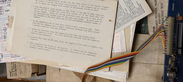 a pile of assorted papers and schematics resting on top of a PCB with a rainbow ribbon cable protruding